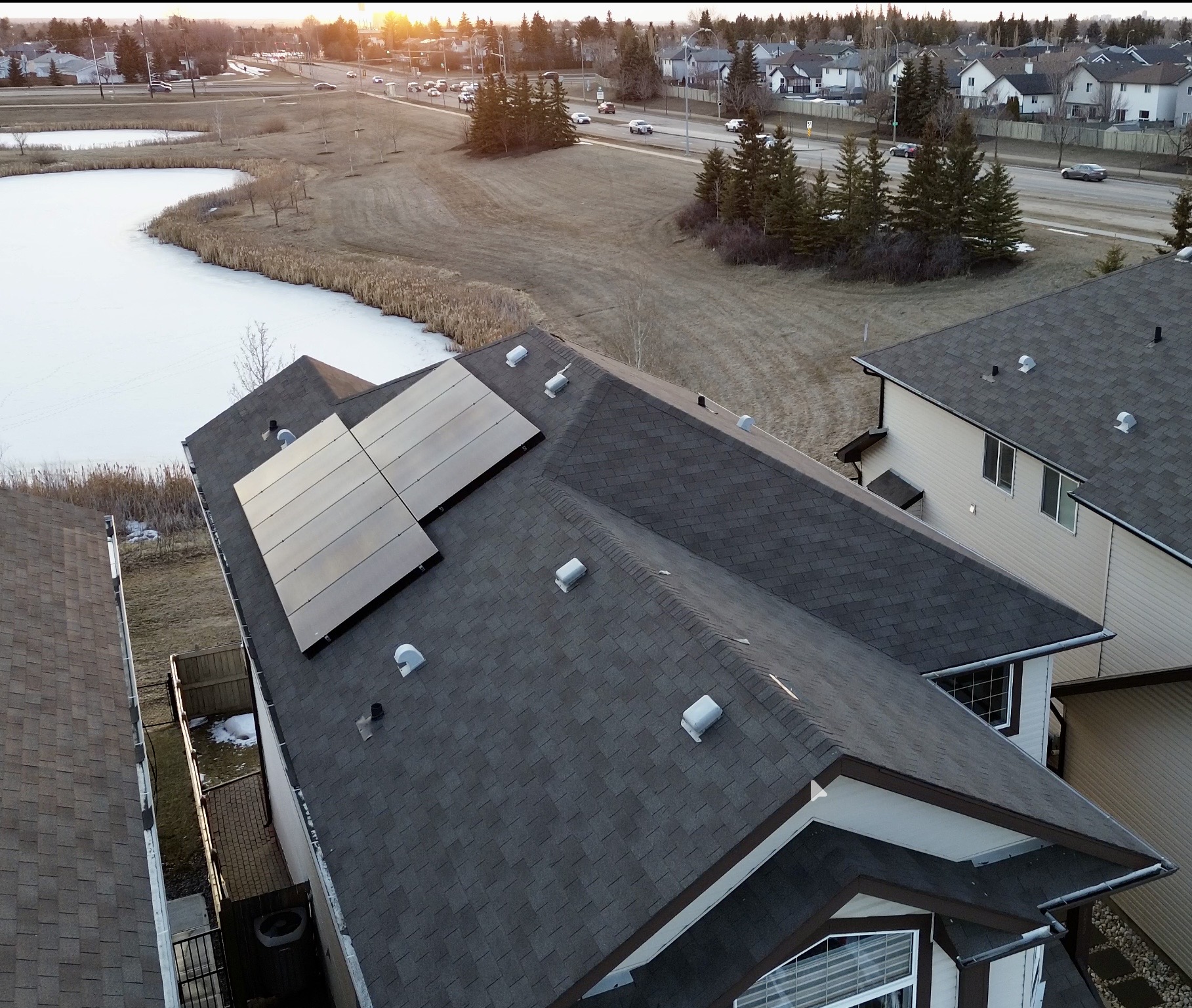 Aerial view of a Stellar Upgrades solar panel installation on an Edmonton home at golden hour with a frozen pond and suburban neighbourhood in the background