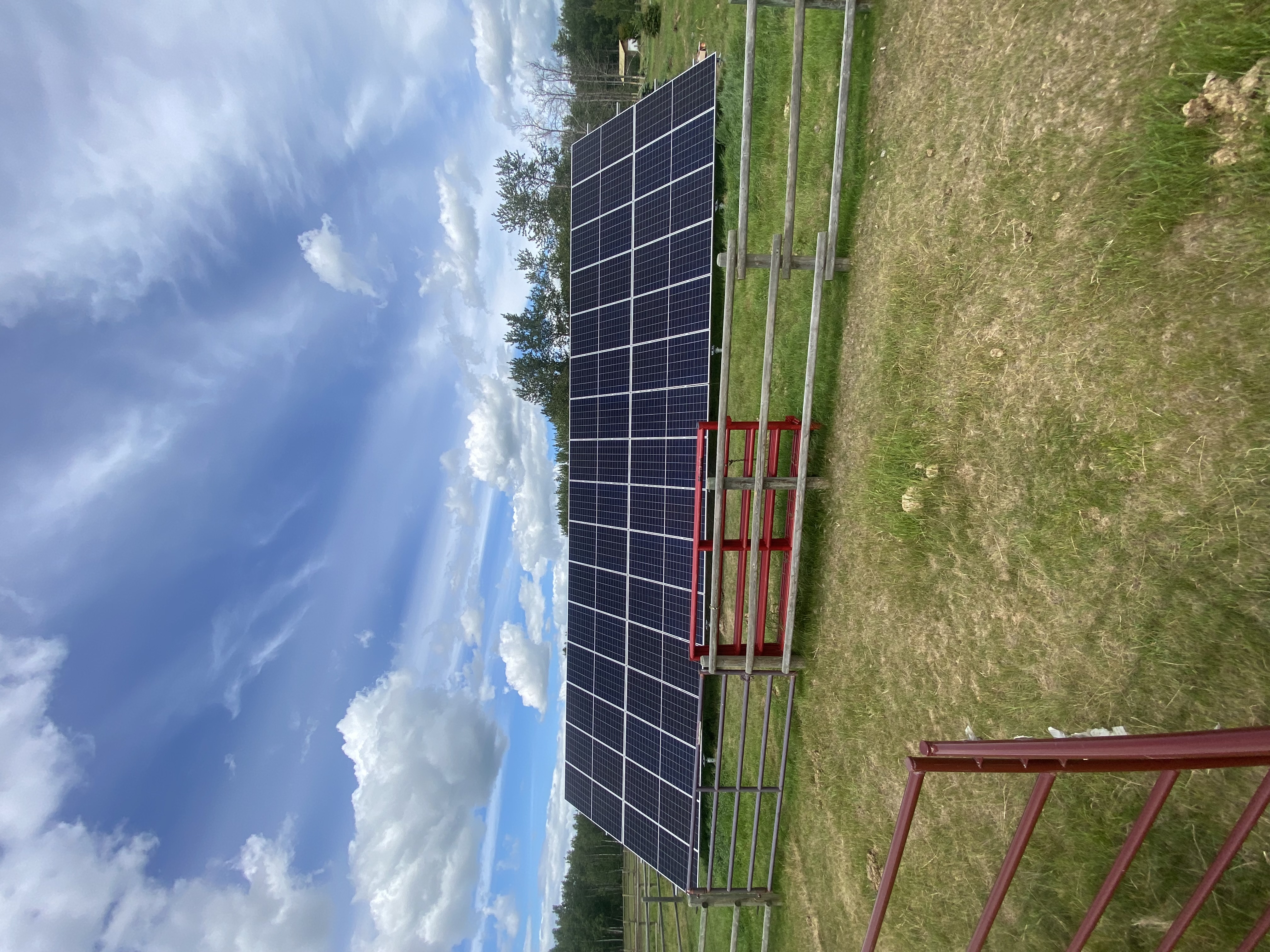 Ground-mount solar array behind red cattle gate on Alberta farm