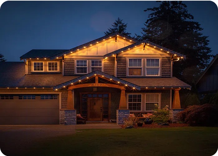 Two-storey craftsman home at dusk with warm white permanent lighting along every roofline and gable