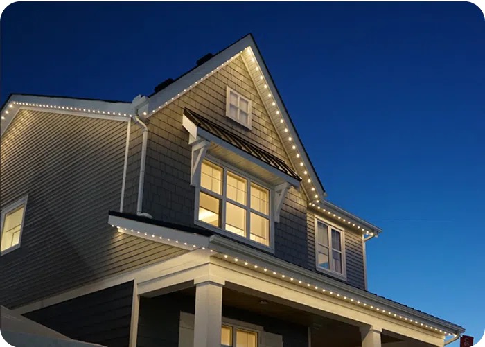 Grey shingle-sided home with white permanent lighting tracing the roof edges and dormer