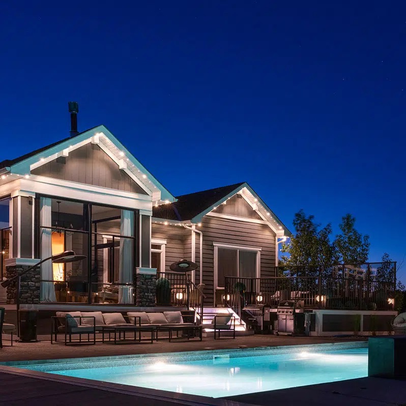Alberta home and backyard pool at dusk with permanent lighting along the rear rooflines